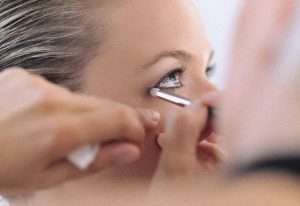 a closeup view of a woman's face while someone is applying eye shadow with a makeup brush to the corner of the left eye.