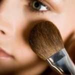 A closeup view of a woman applying powder with a large makeup brush.
