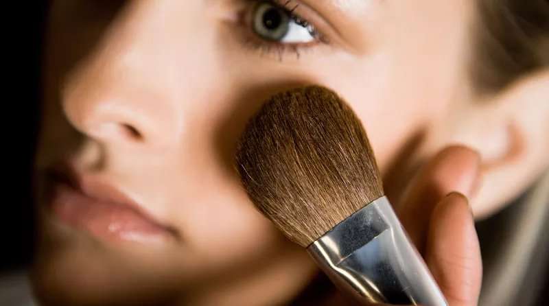 A closeup view of a woman applying powder with a large makeup brush.