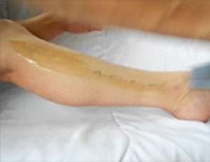 a closeup screenshot from a video depicting sugaring hair removal using denim strips. the screenshot shows the moment when the denim strip is whisked away from the lower inside calf revealing silky smooth skin.