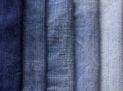 A neatly stacked pile of denim material showcasing various shades and textures, used in making denim strips for sugaring wax bundles.