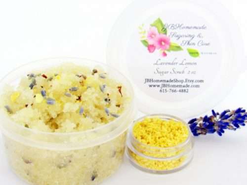 Discover a 2 oz tub of calming cane sugar scrub, a blend of relaxing lavender and invigorating lemon, ideal for a soothing experience. The sugar scrub tub is placed centrally, adorned with dried lemon zest and a lemon slice on top. Flanking the scrub tub is one smaller jar, brimming with dried lemon zest, and a delicate lavender sprig resting in front.