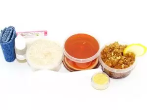 The home sugaring hair removal starter kit comes with a 2 oz tub of soft sugaring wax, a tub of Lemon Zest Sugar Body Scrub, and a tub of Colloidal Oatmeal Brown Sugar Dry Body Scrub, a small bottle of pure aloe vera, a pouch of cornstarch, denim strips, an applicator, and the pristine white surface is garnished with a lemon zest and slices.