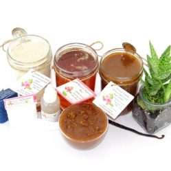 The bundle includes an 8 oz mason jar filled with soft sugaring wax, a jar of Vanilla Aloe Brown Sugar Body Scrub, and Colloidal Oatmeal Brown Sugar Dry Body Scrub, a small bottle of pure aloe vera, a pouch of cornstarch, denim strips, an applicator, and a glass bowl showcasing the sugar scrub, garnished with a vanilla bean and a glass planter with an aloe plant to the right.