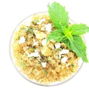 A glass bowl of JBHomemade Sugaring and Skin Care's Natural Peppermint Coconut Sugar Body Scrub with sprinkles of coconut shavings, dried mint and a fresh mint sprig on top.