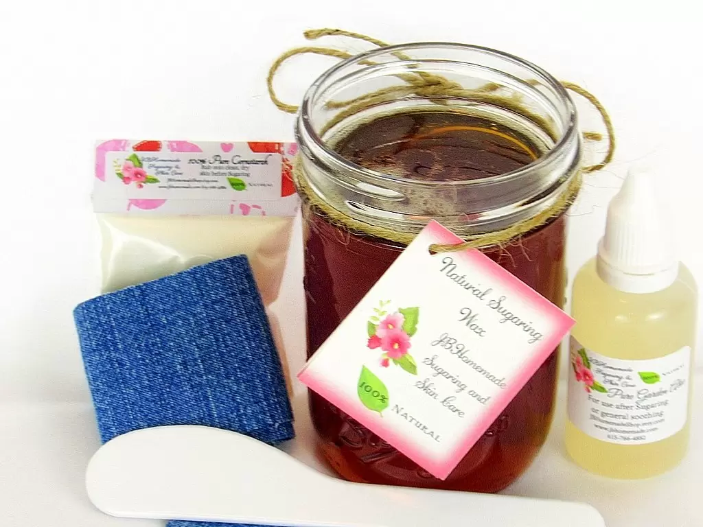 An 8-ounce mason of JBHomemade Sugaring Wax is presented with its included pouch of cornstarch, denim strips, bottle of aloe vera and applicator.