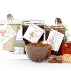 The bundle includes an 8 oz mason jar filled with firm sugaring paste, a jar of Almond Vanilla Brown Sugar Body Scrub, and Colloidal Oatmeal Brown Sugar Dry Body Scrub, a small bottle of pure aloe vera, a pouch of cornstarch, an applicator, and a glass bowl showcasing the sugar scrub, garnished with sprinkled almonds and a small glass jar of raw honey.