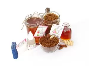 The bundle includes an 8 oz mason jar filled with soft sugaring wax, a jar of Almond Vanilla Brown Sugar Body Scrub, a small bottle of pure aloe vera, a pouch of cornstarch, denim strips, an applicator, and a glass bowl showcasing the sugar scrub, garnished with sprinkled almonds and a small glass jar of raw honey.