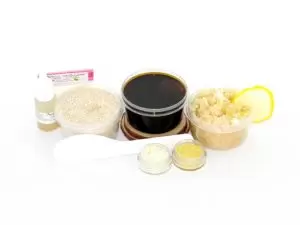 The home sugaring hair removal starter kit comes with a 2 oz tub of firm sugaring paste, a tub of Coconut Lemon Sugar Body Scrub, and a tub of Colloidal Oatmeal Brown Sugar Dry Body Scrub, a small bottle of pure aloe vera, a pouch of cornstarch, an applicator, and the pristine white surface is garnished with coconut shavings, lemon zest and slices.