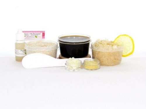 The home sugaring hair removal starter kit comes with a 2 oz tub of firm sugaring paste, a tub of Coconut Lemon Sugar Body Scrub, and a tub of Colloidal Oatmeal Brown Sugar Dry Body Scrub, a small bottle of pure aloe vera, a pouch of cornstarch, an applicator, and the pristine white surface is garnished with coconut shavings, lemon zest and slices.