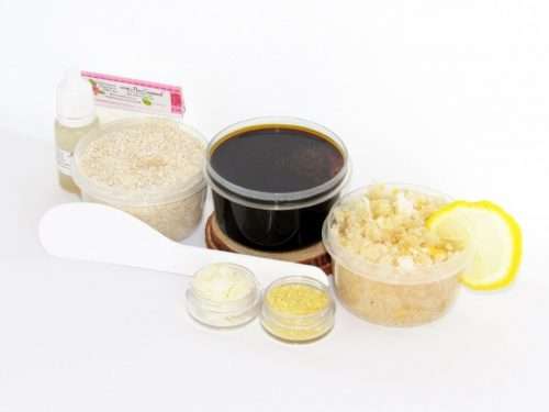 The home sugaring hair removal starter kit comes with a 2 oz tub of firm sugaring paste, a tub of Coconut Lemon Sugar Body Scrub, and a tub of Colloidal Oatmeal Brown Sugar Dry Body Scrub, a small bottle of pure aloe vera, a pouch of cornstarch, an applicator, and the pristine white surface is garnished with coconut shavings, lemon zest and slices.