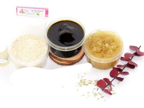The home sugaring hair removal starter kit comes with a 2 oz tub of firm sugaring paste, a tub of Rosemary Eucalyptus Herbal Sugar Body Scrub, and a tub of Colloidal Oatmeal Brown Sugar Dry Body Scrub, a small bottle of pure aloe vera, a pouch of cornstarch, an applicator, and the pristine white surface is garnished with sprinkled dried rosemary and eucalyptus sprigs.