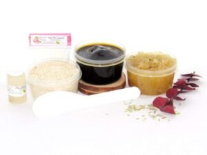 The home sugaring hair removal starter kit comes with a 2 oz tub of firm sugaring paste, a tub of Rosemary Eucalyptus Herbal Sugar Body Scrub, and a tub of Colloidal Oatmeal Brown Sugar Dry Body Scrub, a small bottle of pure aloe vera, a pouch of cornstarch, an applicator, and the pristine white surface is garnished with sprinkled dried rosemary and eucalyptus sprigs.