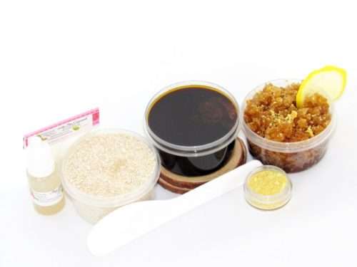 The home sugaring hair removal starter kit comes with a 2 oz tub of firm sugaring paste, a tub of Lemon Zest Sugar Body Scrub, and a tub of Colloidal Oatmeal Brown Sugar Dry Body Scrub, a small bottle of pure aloe vera, a pouch of cornstarch, an applicator, and the pristine white surface is garnished with a lemon zest and slices.