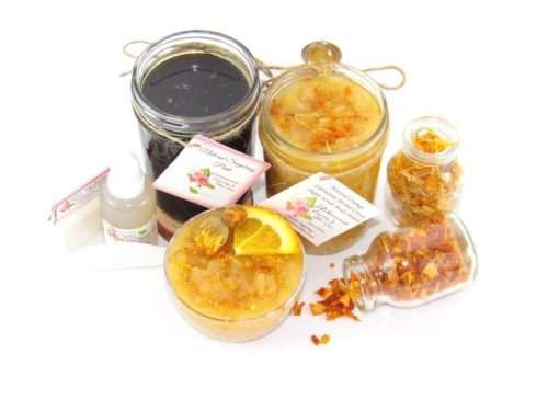 A collection of skincare products including an 8 oz mason jar of sugaring paste and Orange Calendula Herbal Sugar Scrub, accompanied by smaller jars of calendula petals and dried orange zest on a white background.