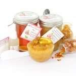 A collection of skincare products including an 8 oz mason jar of sugaring wax and Orange Calendula Herbal Sugar Scrub, the included applicator, bottle of pure aloe vera, denims strips and accompanied by smaller jars of calendula petals and dried orange zest on a white background.