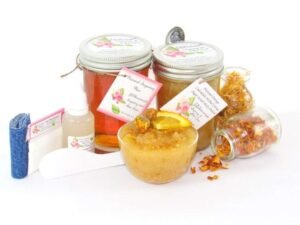 A collection of skincare products including an 8 oz mason jar of sugaring wax and Orange Calendula Herbal Sugar Scrub, the included applicator, bottle of pure aloe vera, denims strips and accompanied by smaller jars of calendula petals and dried orange zest on a white background.