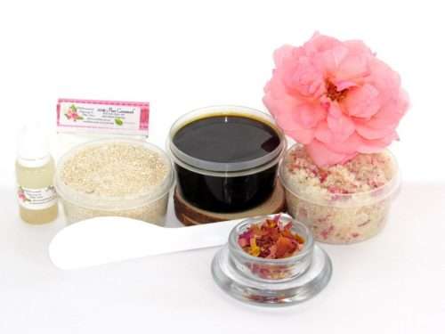 The home sugaring hair removal starter kit comes with a 2 oz tub of firm sugaring paste, a tub of Pink Rose Petal Sugar Body Scrub, and a tub of Colloidal Oatmeal Brown Sugar Dry Body Scrub, a small bottle of pure aloe vera, a pouch of cornstarch, an applicator, and a glass bowl garnished with a pink rose bloom.