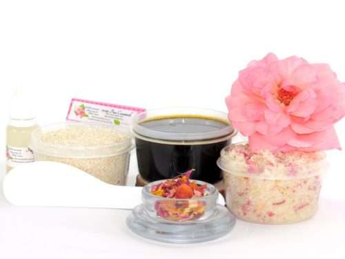 The home sugaring hair removal starter kit comes with a 2 oz tub of firm sugaring paste, a tub of Pink Rose Petal Sugar Body Scrub, and a tub of Colloidal Oatmeal Brown Sugar Dry Body Scrub, a small bottle of pure aloe vera, a pouch of cornstarch, an applicator, and a glass bowl garnished with a pink rose bloom.