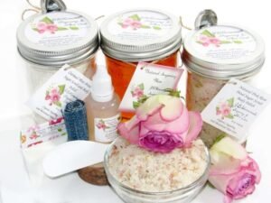 The bundle includes an 8 oz mason jar filled with soft sugaring wax, a jar of Pink Rose Petal Sugar Body Scrub, and Colloidal Oatmeal Brown Sugar Dry Body Scrub, a small bottle of pure aloe vera, a pouch of cornstarch, denim strips, an applicator, and a glass bowl showcasing the sugar scrub, garnished with a pink rose bloom.