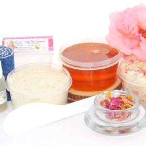 The home sugaring hair removal starter kit comes with a 2 oz tub of soft sugaring wax, a tub of Pink Rose Petal Sugar Body Scrub, and a tub of Colloidal Oatmeal Brown Sugar Dry Body Scrub, a small bottle of pure aloe vera, a pouch of cornstarch, denim strips, an applicator, and a glass bowl garnished with a pink rose bloom.