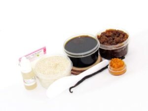 The home sugaring hair removal starter kit comes with a 2 oz tub of firm sugaring paste, a tub of Pumpkin Vanilla Brown Sugar Body Scrub, and a tub of Colloidal Oatmeal Brown Sugar Dry Body Scrub, a small bottle of pure aloe vera, a pouch of cornstarch, an applicator, and the pristine white surface is garnished with a vanilla bean and pumpkin puree.