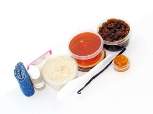 The home sugaring hair removal starter kit comes with a 2 oz tub of soft sugaring wax, a tub of Pumpkin Vanilla Brown Sugar Body Scrub, and a tub of Colloidal Oatmeal Brown Sugar Dry Body Scrub, a small bottle of pure aloe vera, a pouch of cornstarch, denim strips, an applicator, and the pristine white surface is garnished with a vanilla bean and pumpkin puree.
