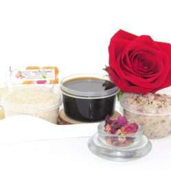 The home sugaring hair removal starter kit comes with a 2 oz tub of firm sugaring paste, a tub of Red Rose Petal Sugar Body Scrub, and a tub of Colloidal Oatmeal Brown Sugar Dry Body Scrub, a small bottle of pure aloe vera, a pouch of cornstarch, an applicator, and a glass bowl garnished with a red rose bloom.