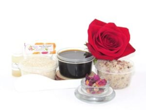 The home sugaring hair removal starter kit comes with a 2 oz tub of firm sugaring paste, a tub of Red Rose Petal Sugar Body Scrub, and a tub of Colloidal Oatmeal Brown Sugar Dry Body Scrub, a small bottle of pure aloe vera, a pouch of cornstarch, an applicator, and a glass bowl garnished with a red rose bloom.