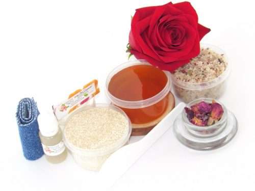 The home sugaring hair removal starter kit comes with a 2 oz tub of soft sugaring wax, a tub of Red Rose Petal Sugar Body Scrub, and a tub of Colloidal Oatmeal Brown Sugar Dry Body Scrub, a small bottle of pure aloe vera, a pouch of cornstarch, denim strips, an applicator, and a glass bowl garnished with a red rose bloom.
