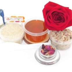 The home sugaring hair removal starter kit comes with a 2 oz tub of soft sugaring wax, a tub of Red Rose Petal Sugar Body Scrub, and a tub of Colloidal Oatmeal Brown Sugar Dry Body Scrub, a small bottle of pure aloe vera, a pouch of cornstarch, denim strips, an applicator, and a glass bowl garnished with a red rose bloom.