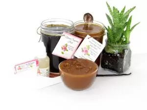 The bundle includes an 8 oz mason jar filled with firm sugaring paste, a jar of Vanilla Aloe Brown Sugar Body Scrub, a small bottle of pure aloe vera, a pouch of cornstarch, an applicator, and a glass bowl showcasing the sugar scrub, garnished with a vanilla bean and a glass planter with an aloe plant to the right.