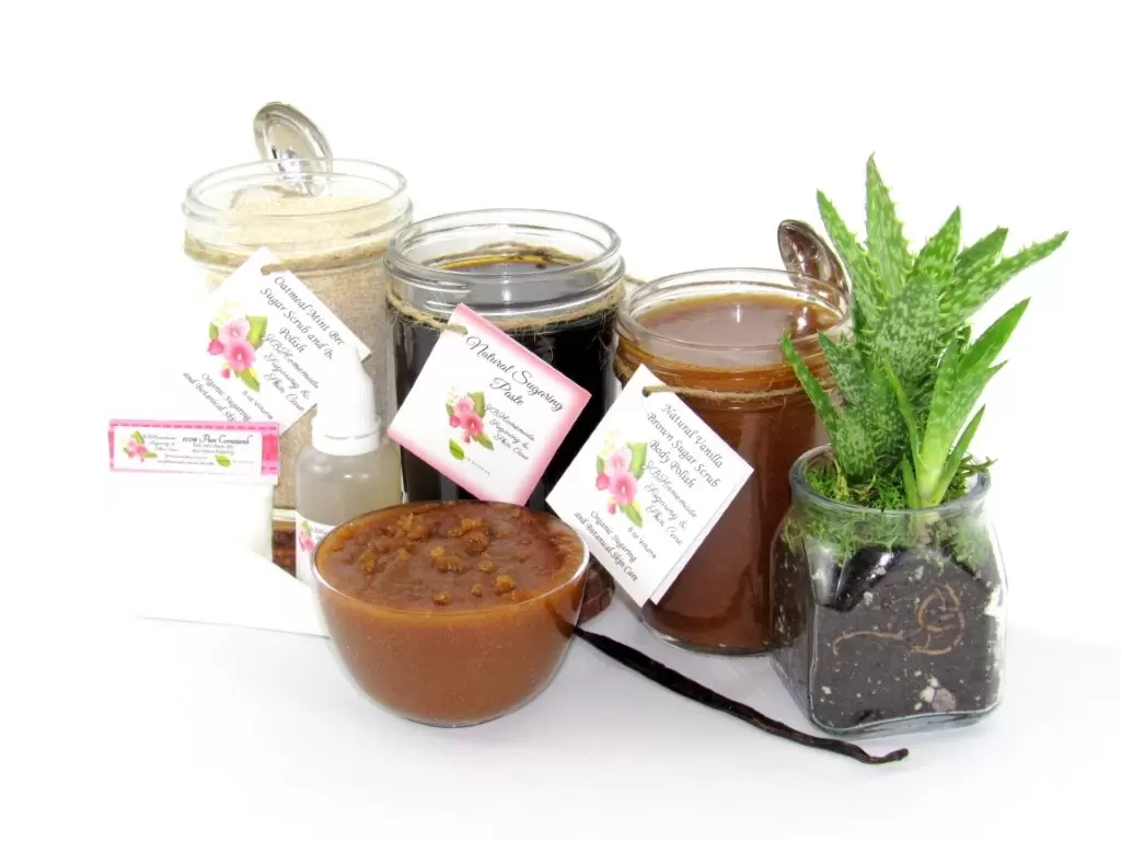 The bundle includes an 8 oz mason jar filled with firm sugaring paste, a jar of Vanilla Aloe Brown Sugar Body Scrub, and Colloidal Oatmeal Brown Sugar Dry Body Scrub, a small bottle of pure aloe vera, a pouch of cornstarch, an applicator, and a glass bowl showcasing the sugar scrub, garnished with a vanilla bean and a glass planter with an aloe plant to the right.
