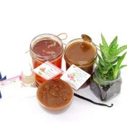The bundle includes an 8 oz mason jar filled with soft sugaring wax, a jar of Vanilla Aloe Brown Sugar Body Scrub, a small bottle of pure aloe vera, a pouch of cornstarch, denim strips, an applicator, and a glass bowl showcasing the sugar scrub, garnished with a vanilla bean and a glass planter with an aloe plant to the right.