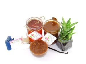 The bundle includes an 8 oz mason jar filled with soft sugaring wax, a jar of Vanilla Aloe Brown Sugar Body Scrub, a small bottle of pure aloe vera, a pouch of cornstarch, denim strips, an applicator, and a glass bowl showcasing the sugar scrub, garnished with a vanilla bean and a glass planter with an aloe plant to the right.