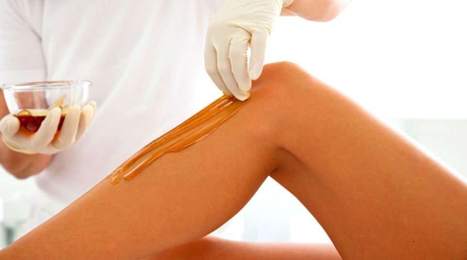 A close-up view of a person applying sugaring paste for hair removal on their leg