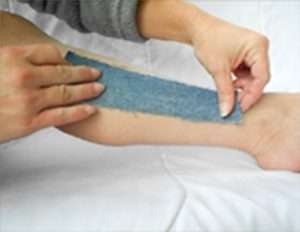 Application of denim strip over warm, soft sugaring wax on skin.