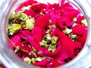 A glass jar filled to the brim with a colorful mix of red rose petals and chamomile flowers.