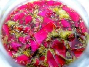 The grapeseed oil begins to infuse, capturing the essence of the red roses and chamomile in the jar.