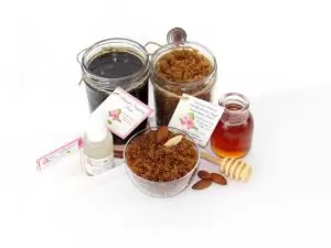 The bundle includes an 8 oz mason jar filled with firm sugaring paste, a jar of Almond Vanilla Brown Sugar Body Scrub, a small bottle of pure aloe vera, a pouch of cornstarch, an applicator, and a glass bowl showcasing the sugar scrub, garnished with sprinkled almonds and a small glass jar of raw honey.