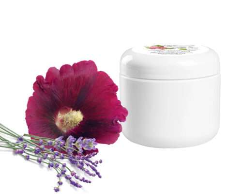 A dark pink hollyhock flower, seen from the front, is accompanied by some lavender sprigs and a jar of natural clay facial mask. The mask is made with garden-fresh ingredients, including lavender, hollyhock and aloe. It hydrates the skin and gives it a radiant glow. The jar contains 2 oz of the product.
