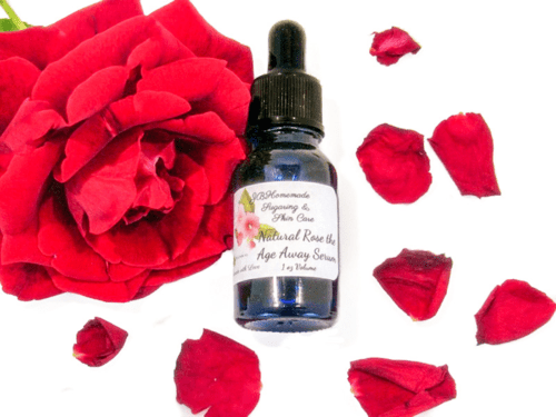A serum bottle containing JBHomemade Sugaring and Skin Care's natural Rose the Age Away Serum is next to a vivid red rose in this image.