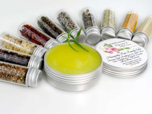 Small glass jars containing ground cloves, turmeric, ginger, St. John’s Wort, frankincense, sandalwood, patchouli, lavender, ylang-ylang extra, and rosemary, arranged around the Comfort Harmony Salve tin.