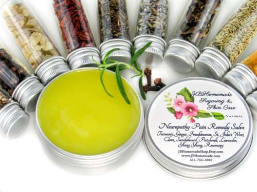 Small glass jars containing ground cloves, turmeric, ginger, St. John’s Wort, frankincense, sandalwood, patchouli, lavender, ylang-ylang extra, and rosemary, arranged around the Comfort Harmony Salve tin.