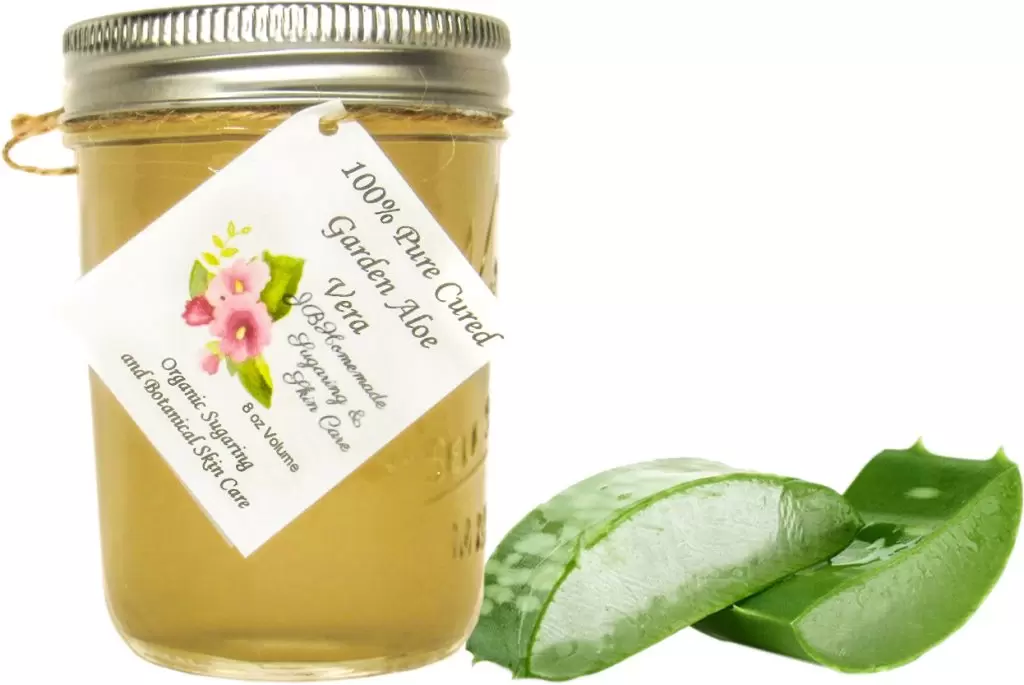 An 8 oz glass mason jar filled with pure aloe vera gel, adorned with a hangtag and placed next to fresh slices of aloe vera leaf, showcasing the natural and organic ingredients.