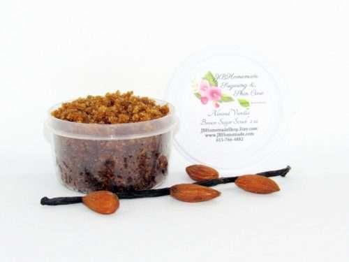 Centered is a 2 oz tub of natural brown sugar body scrub, enriched with almond, honey, and vanilla. In the foreground lies scattered almonds and a whole vanilla bean.