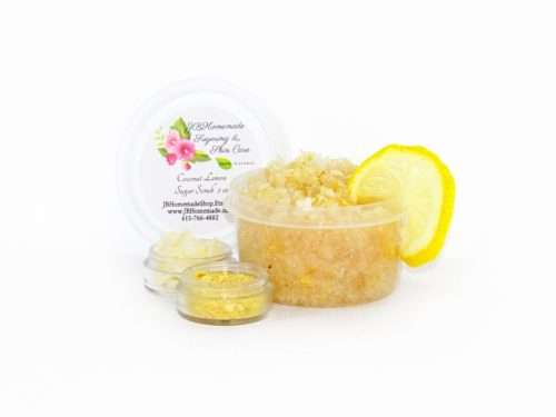 A 2 oz tub of cane sugar scrub is infused with coconut essence and zesty lemon. The sugar scrub tub is centered, topped with dried lemon zest and a slice of lemon. To the left, two tiny glass bowls filled with coconut shavings and dried lemon zest.