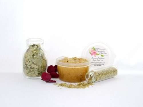A 2 oz tub of refreshing herbal cane sugar scrub is infused with rosemary and eucalyptus, perfect for rejuvenating weary skin. The accompanying image shows the scrub tub centrally placed, flanked by two smaller glass jars—one filled with dried rosemary, the other with dried eucalyptus—both tipped over, their contents scattered on a pristine white surface. Beside the jar lies a sprig of dried eucalyptus.