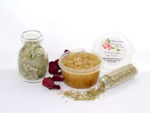 A 2 oz tub of refreshing herbal cane sugar scrub is infused with rosemary and eucalyptus, perfect for rejuvenating weary skin. The accompanying image shows the scrub tub centrally placed, flanked by two smaller glass jars—one filled with dried rosemary, the other with dried eucalyptus—both tipped over, their contents scattered on a pristine white surface. Beside the jar lies a sprig of dried eucalyptus.