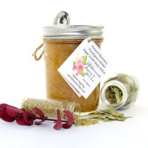 An 8 oz jar of refreshing herbal cane sugar scrub is infused with rosemary and eucalyptus, perfect for rejuvenating weary skin. The accompanying image shows the scrub jar centrally placed, flanked by two smaller glass jars—one filled with dried rosemary, the other with dried eucalyptus—both tipped over, their contents scattered on a pristine white surface. Beside the jar lies a sprig of dried eucalyptus.